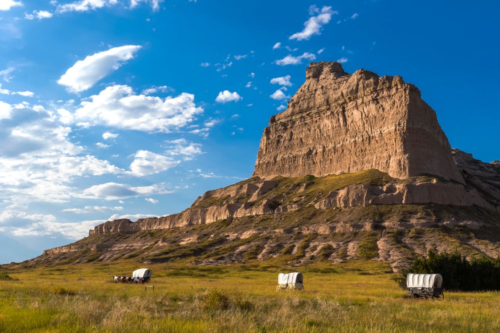 Photo of covered wagons traveling through the prairie with a mountain in the background
