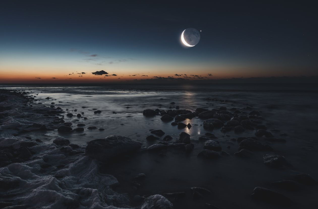 Photo of a the moon in a dark sky above a rocky coast