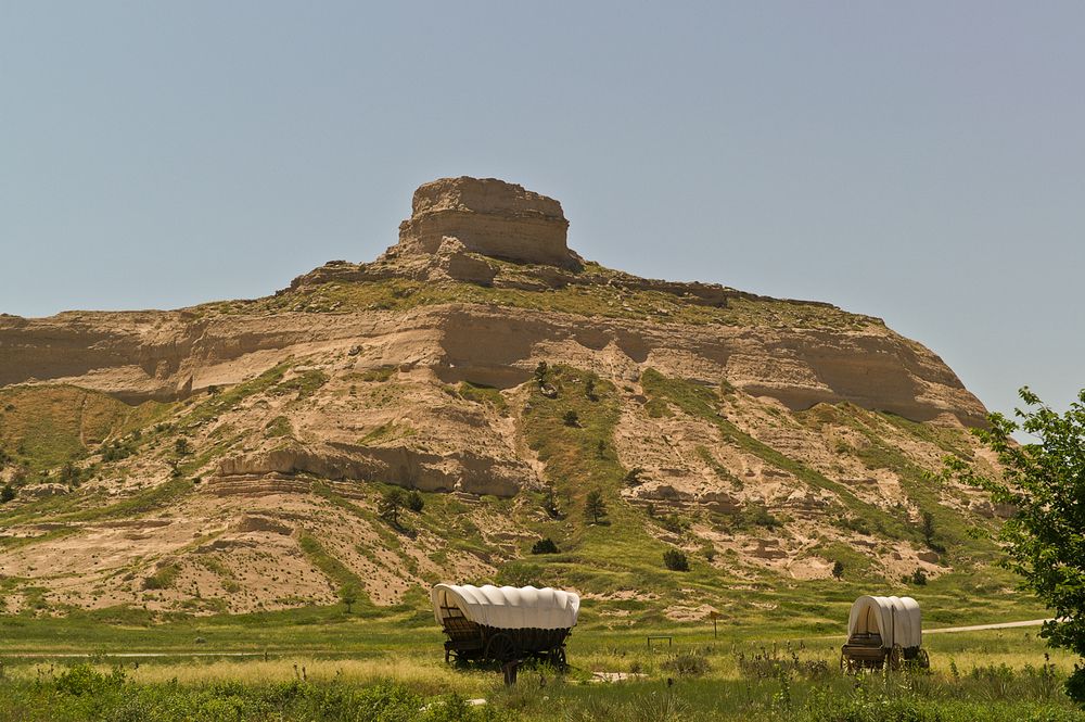 Covered wagons move across the plains with large rocky hills in the background