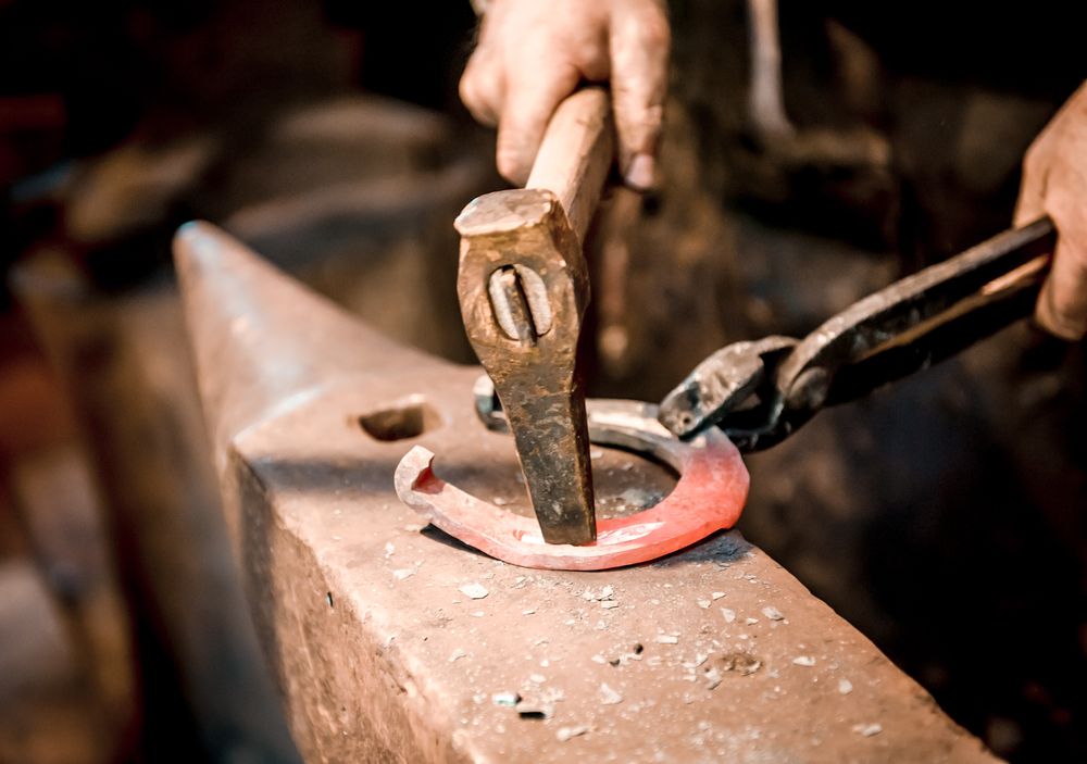 Blacksmith holding tongs and hammer, pressing horseshoe into shape