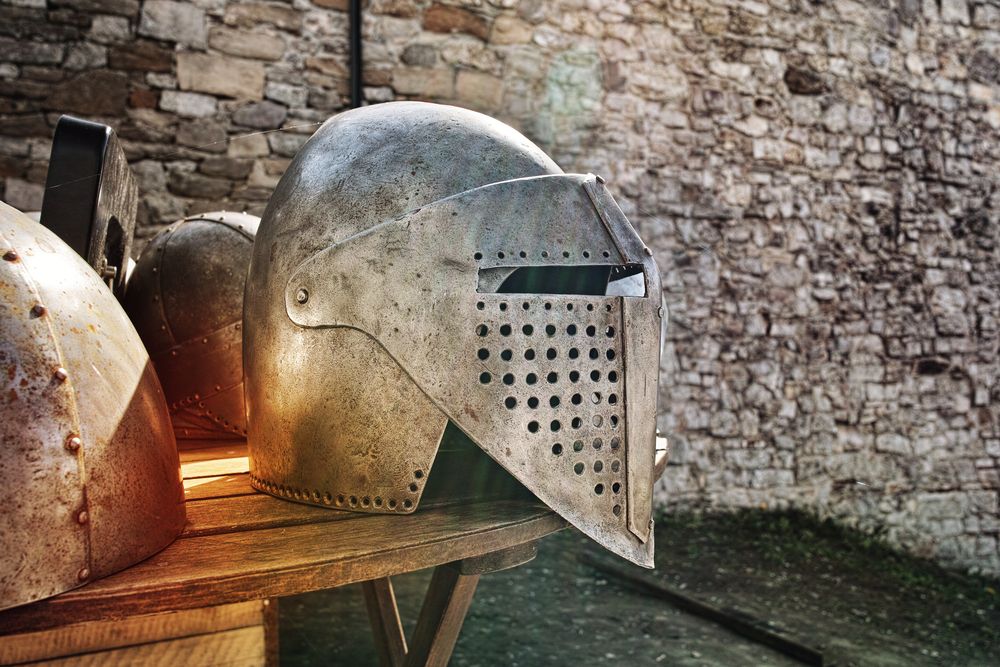 Traditional iron knight's helmet resting on bench near a stony castle wall