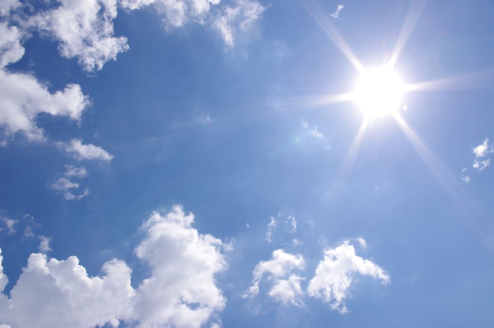 Bright sun shining against blue sky with scattered clouds