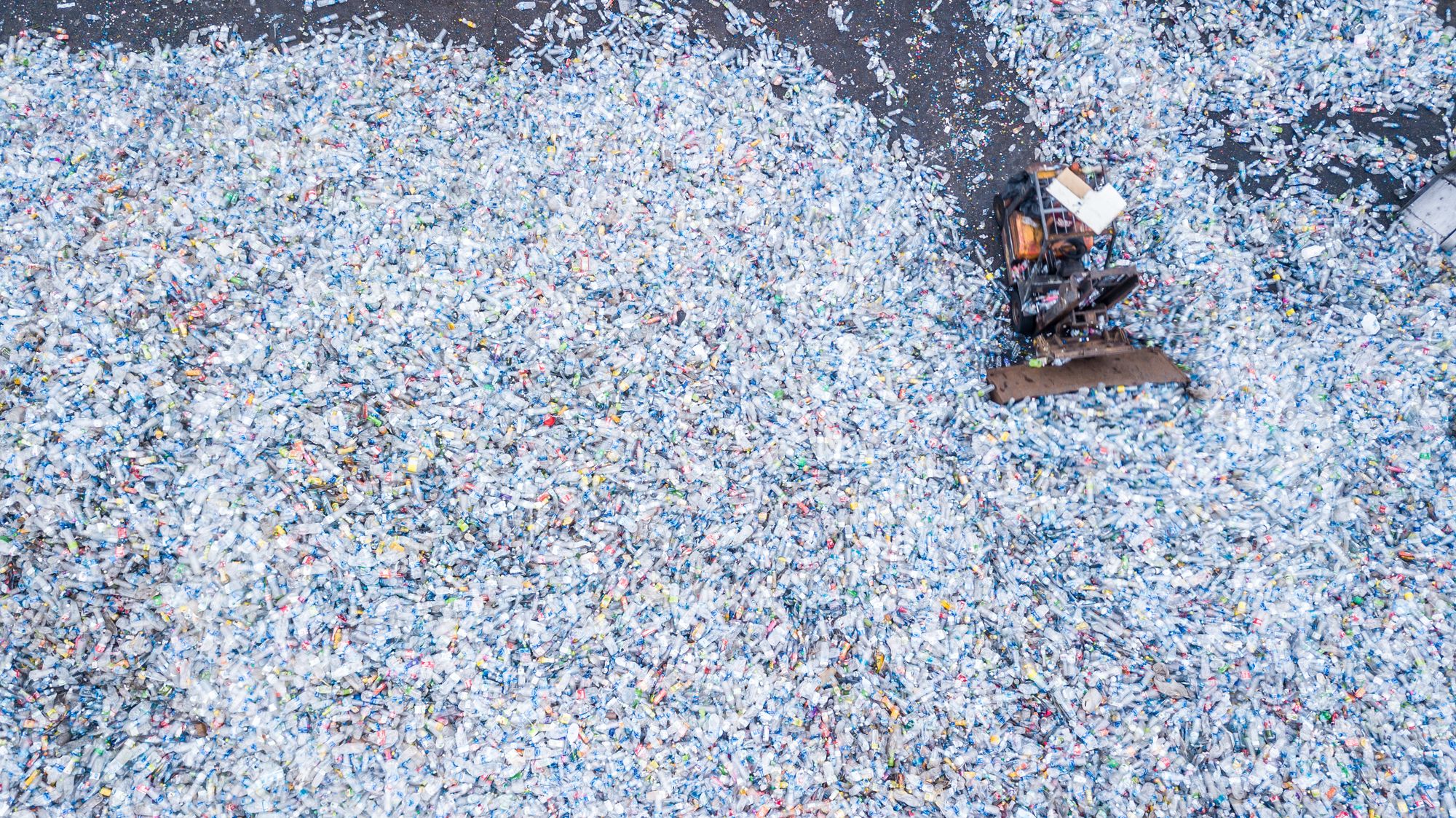 Aerial view of large bulldozer moving huge piles of plastic bottles in a landfill
