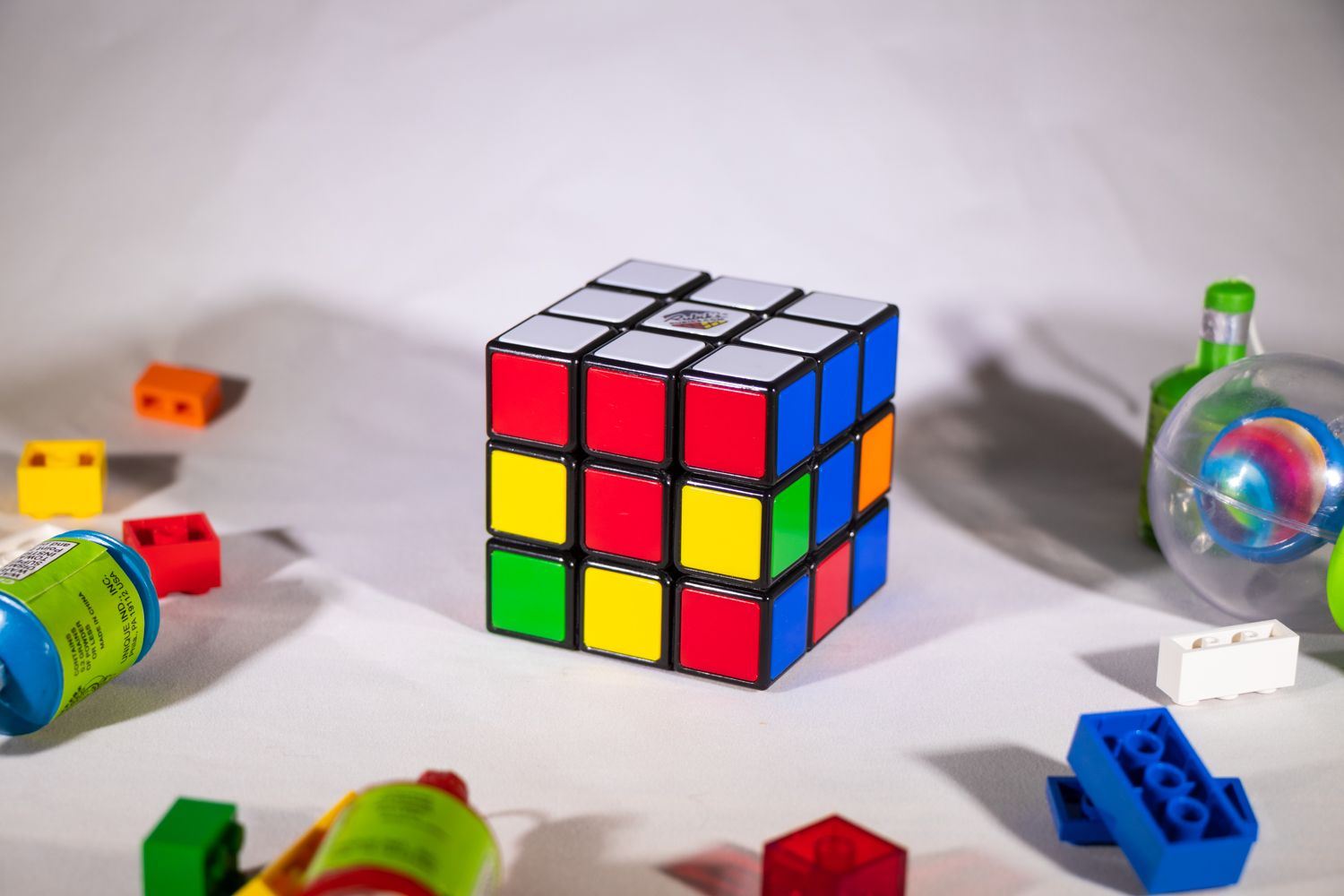 Rubik's Cube on white surface in progress, with scattered toys nearby
