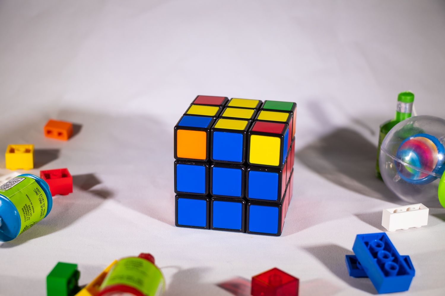 Rubik's Cube on white table nearing completion, surrounded by LEGO and toys