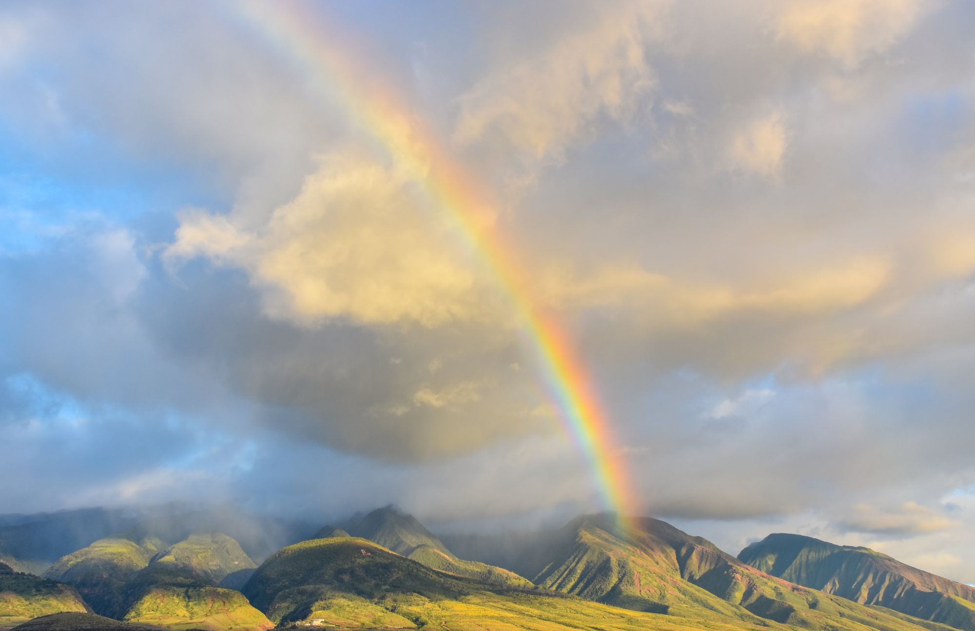 Rainbow over green mountains with clouds in Hawaii