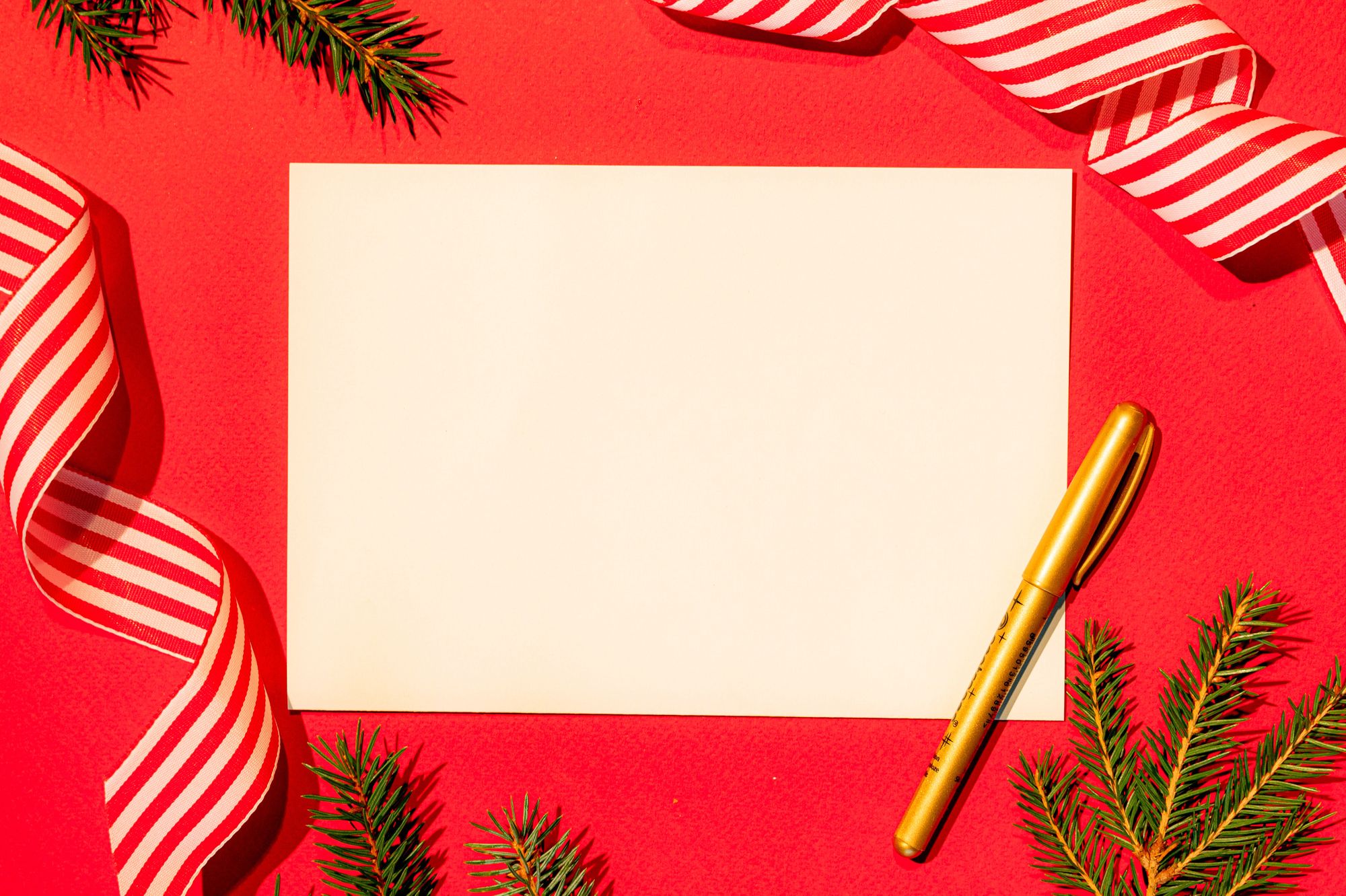 An empty card with a gold pen on a red background with fir branches and stripped ribbon
