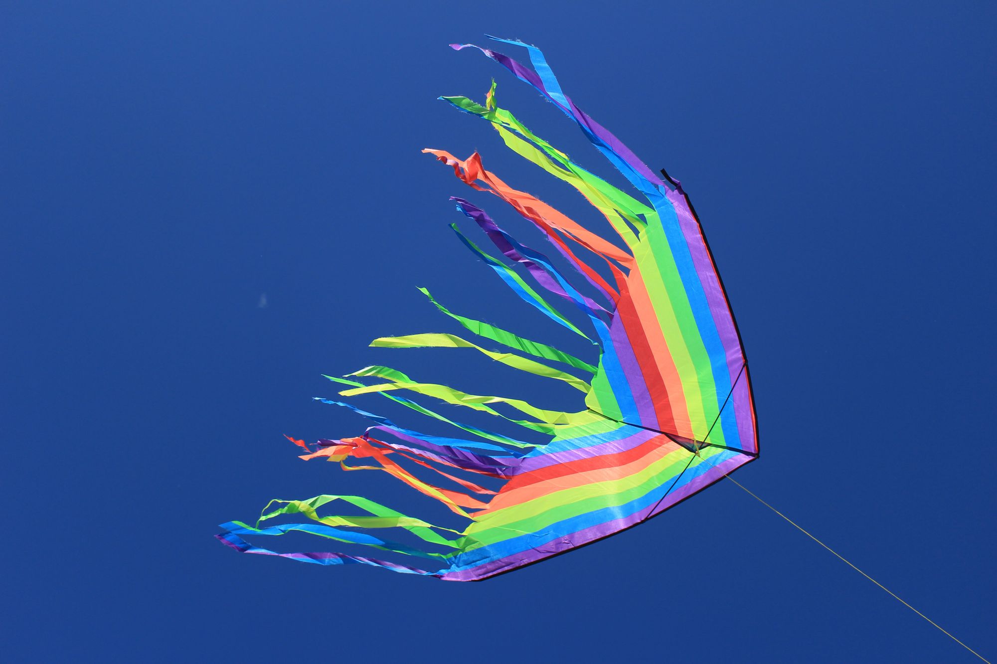 Rainbow colored kite being flown on a blue sky day