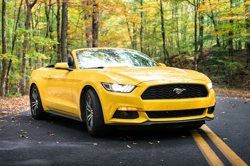A yellow convertible Ford Mustang in the middle of a road.