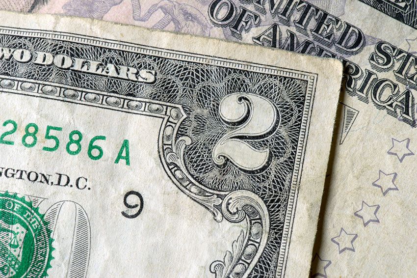 Close up of the top corner of a two dollar billing on top of another bill.