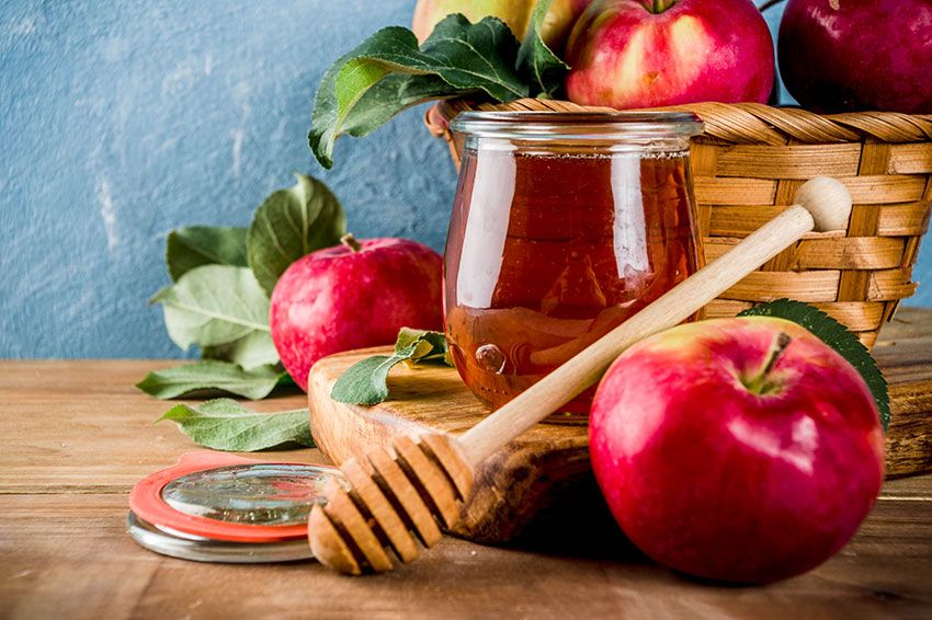 Red apples, apple leaves and honey in jar on a wooden surface.