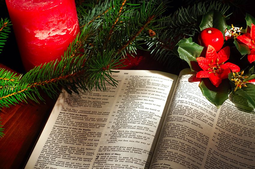 Bible open to the Christmas passage of Luke 2 with evergreen sprigs, candle, and poinsettia decor.