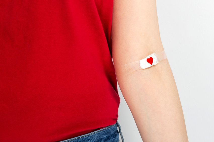 Young girl in red T-shirt hand taped with patch with red heart after giving blood.