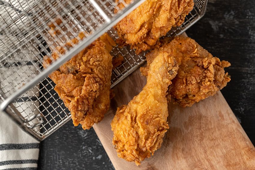 Fried chicken spilling out of a fryer basket on to a cutting board. 