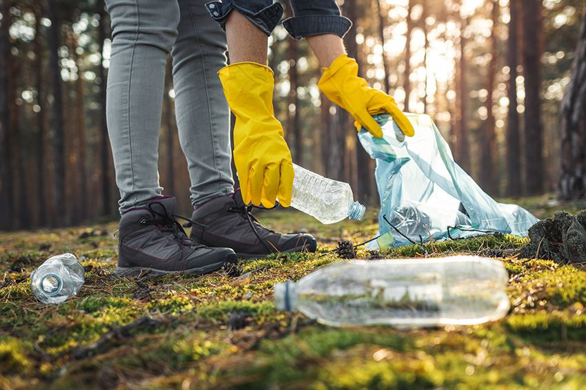 Hands with protective glove picking up plastic bottles in a park.