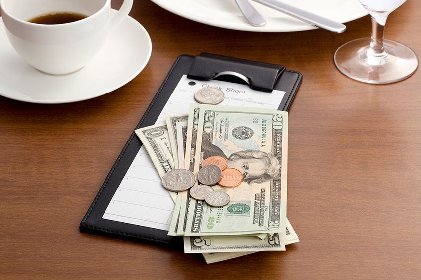 Restaurant check with money on top surrounded by dishes.