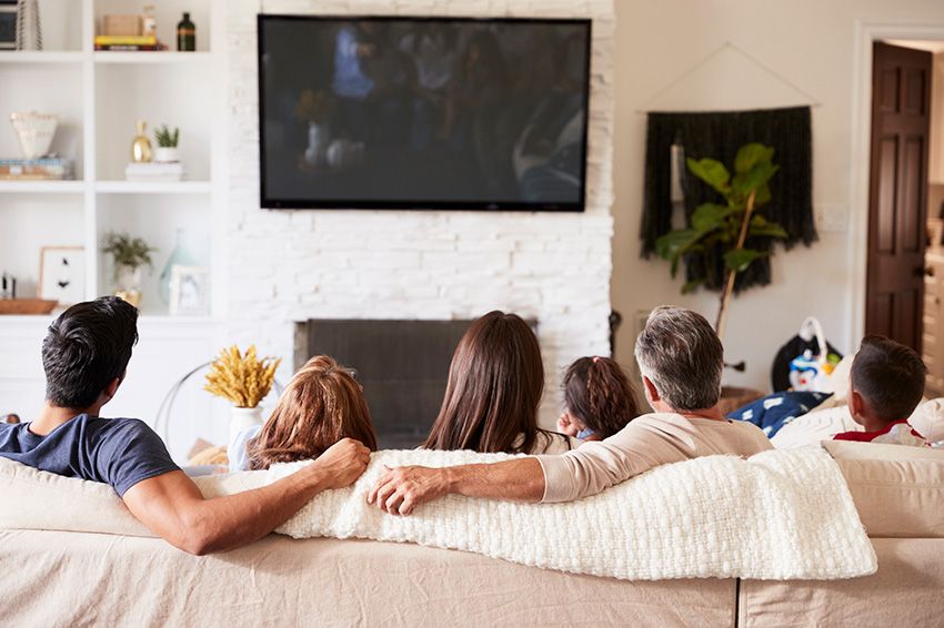 A family from behind sitting on a couch watching tv.